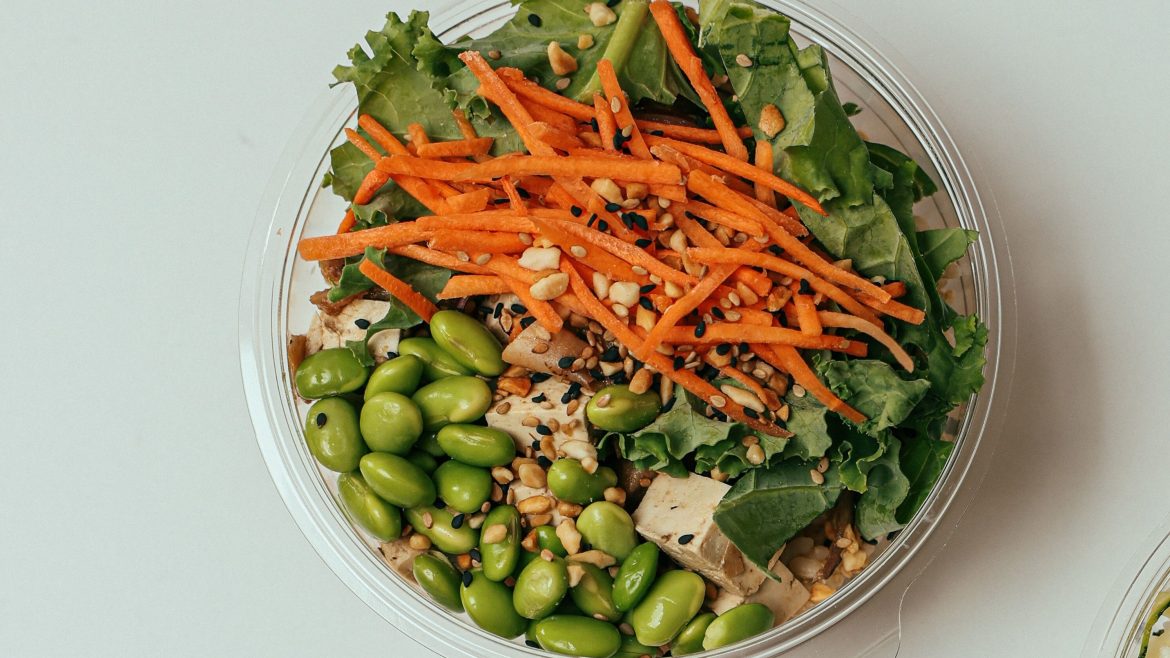 A close up image of a Tofu and Edamame salad bowl, topped with carrot and leafy greens.