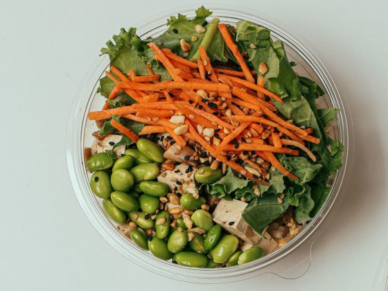 A close up image of a Tofu and Edamame salad bowl, topped with carrot and leafy greens.