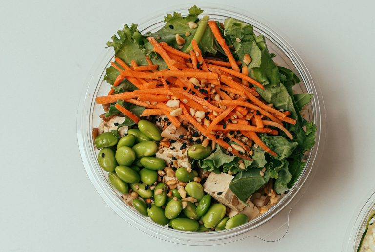 A close up image of a Tofu and Edamame salad bowl, topped with carrot and leafy greens.