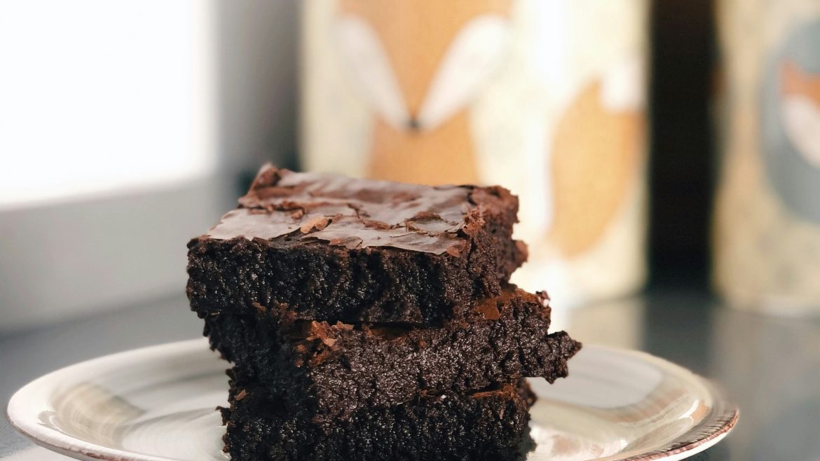 A medium close up shot of three stacked brownies on a plate.